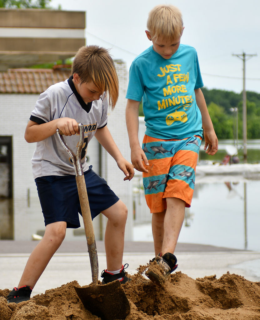 Friends Ashton Bucholc and Isaak Rand kick and shovel dirt to loosen it up to fill sandbags